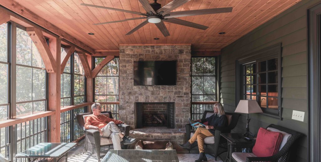 A covered lake-house porch with a stone fireplace, enclosed with Porch Conversions windows